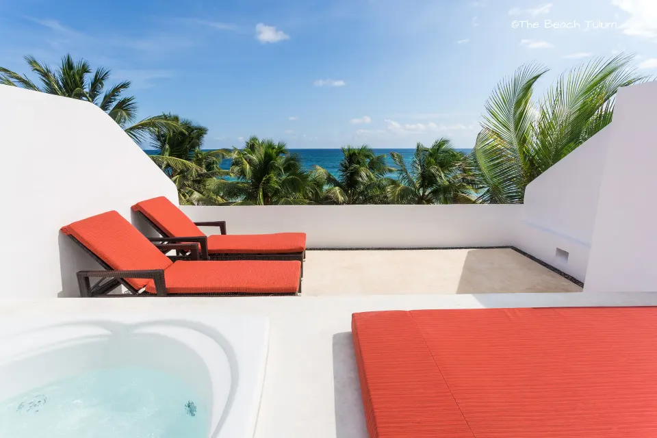 Rooftop jacuzzi and loungers with palm trees and sea beyond at The Beach Tulum