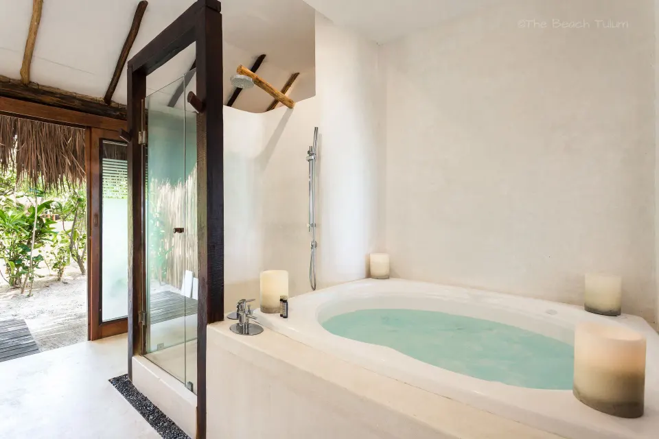 Soaking tub and glass shower doorway in a Junior Suite bathroom at The Beach Tulum.