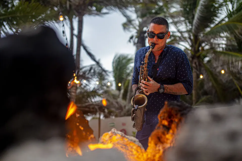 Saxophonist playing by a beachfront fire pit at The Beach Tulum