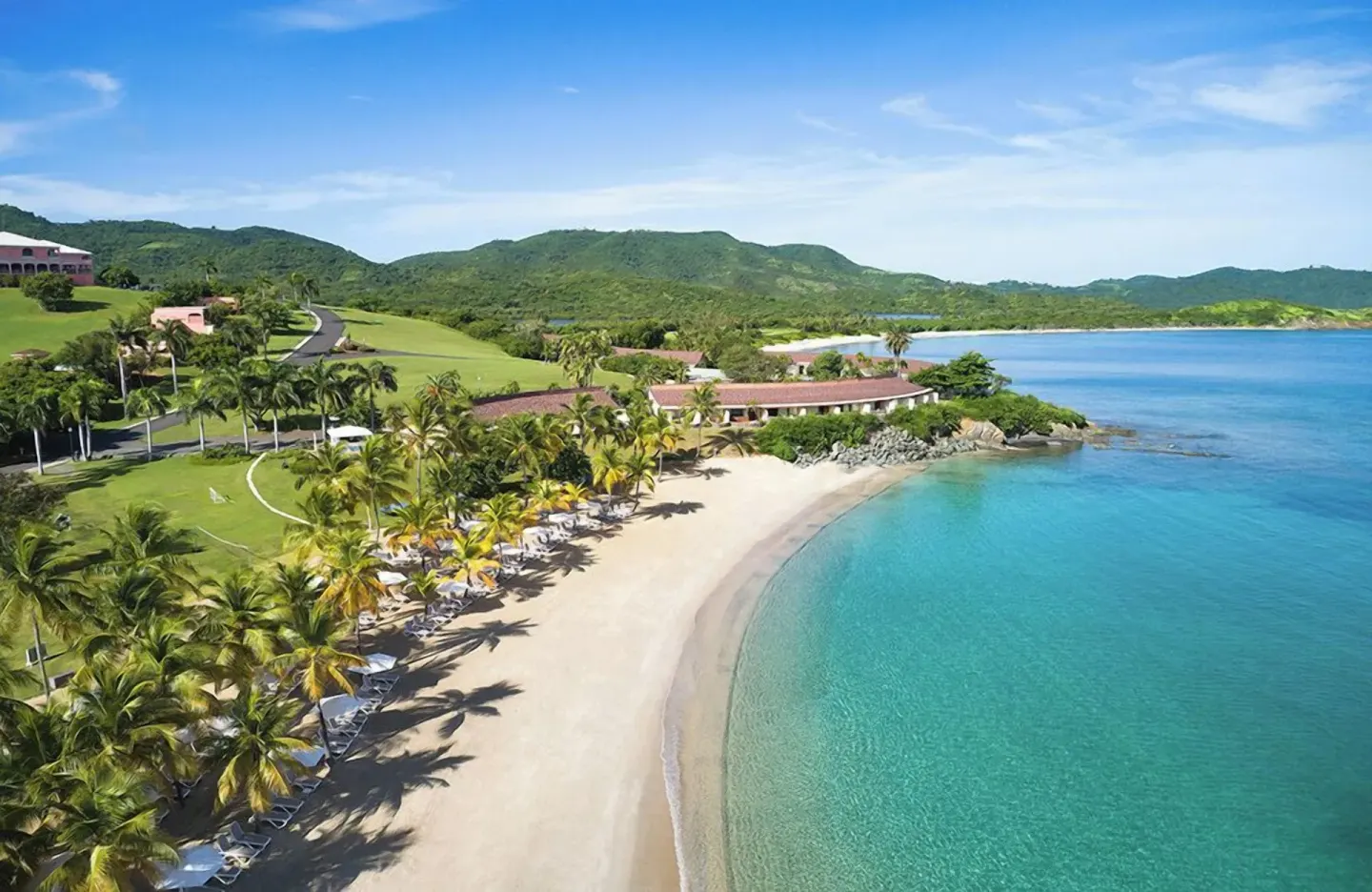 Aerial view of the beach, palms, and turquoise bay at The Buccaneer Beach & Golf Resort.