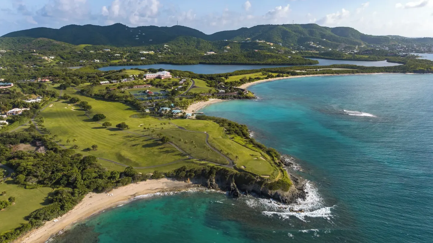 Aerial coastline, golf greens, beaches, and bay at The Buccaneer Beach & Golf Resort.
