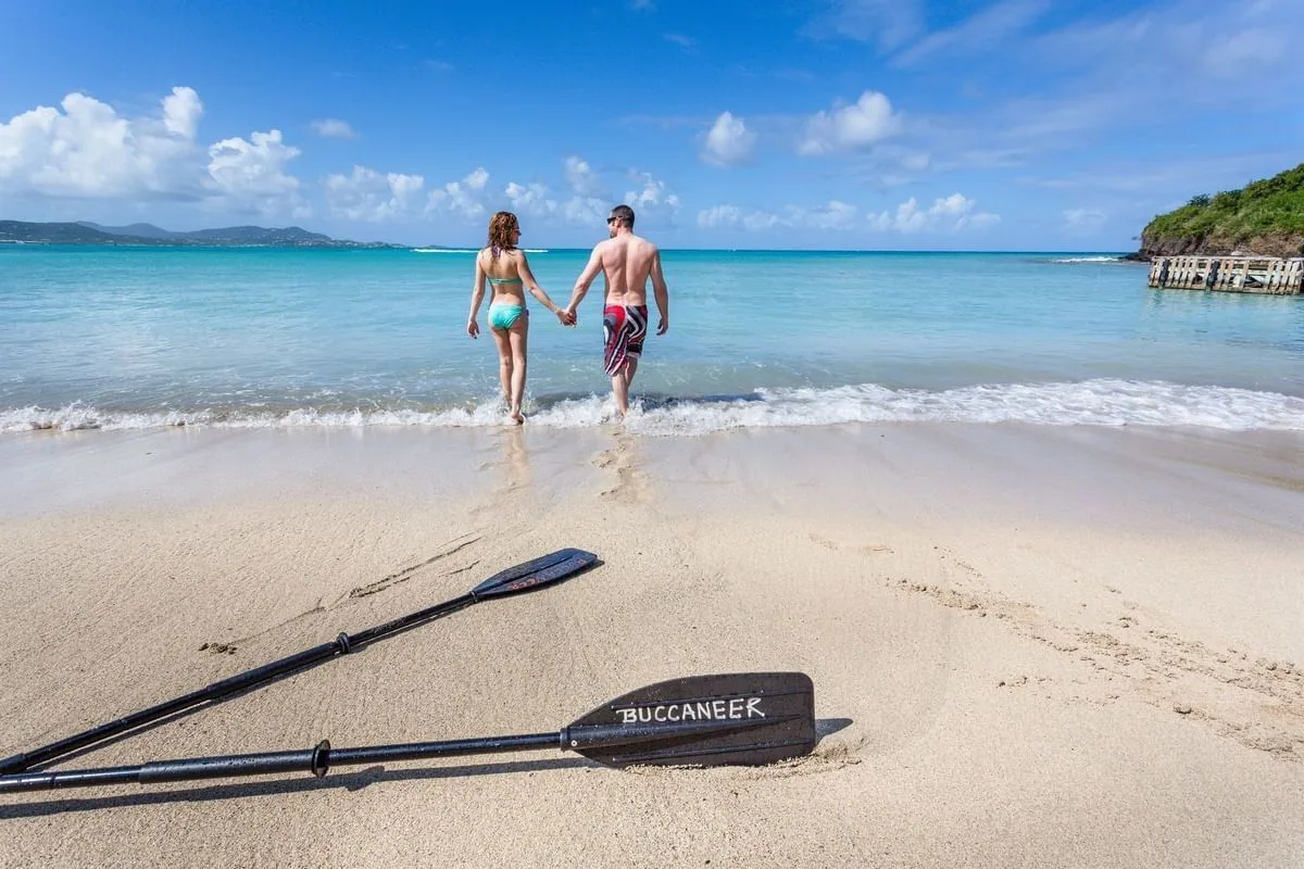 Two guests walk into the surf beside paddles at The Buccaneer Beach & Golf Resort.