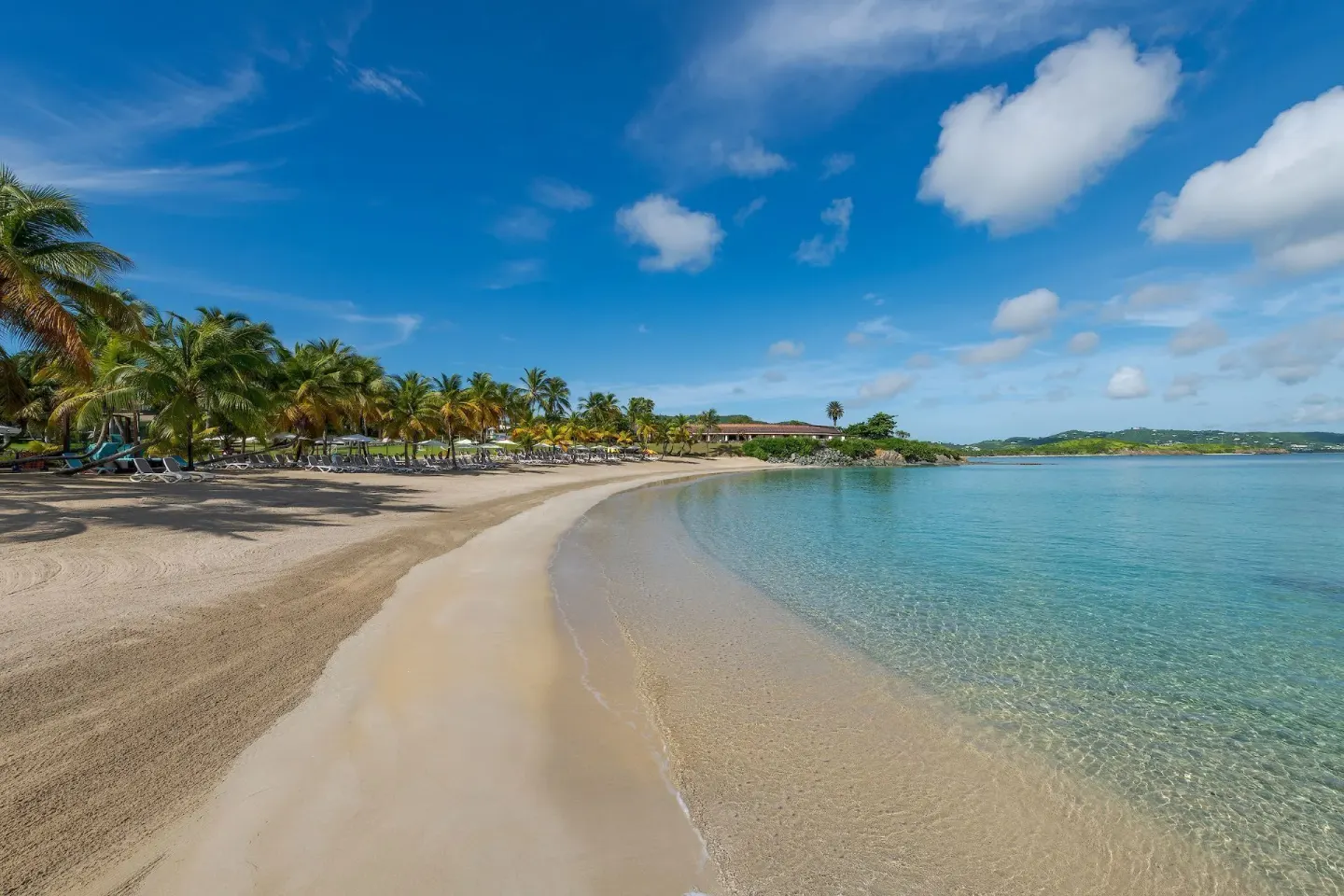 Curving sandy beach with calm clear water at The Buccaneer Beach & Golf Resort.