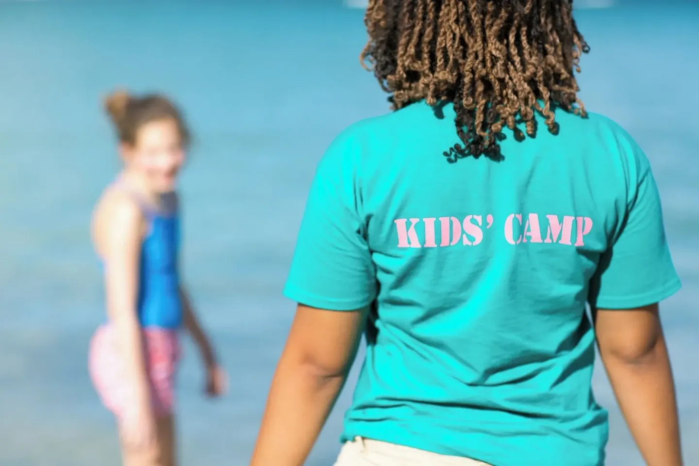 Kids' camp staff member by the water with a child at The Buccaneer Beach & Golf Resort.