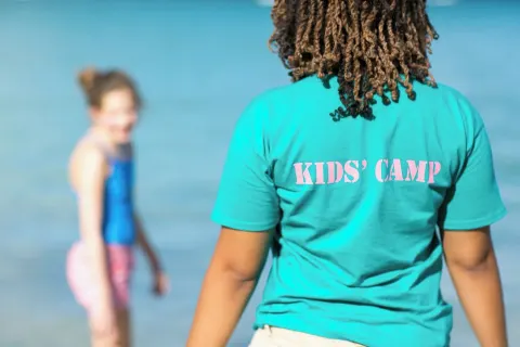 Kids' camp staff member by the water with a child at The Buccaneer Beach & Golf Resort.