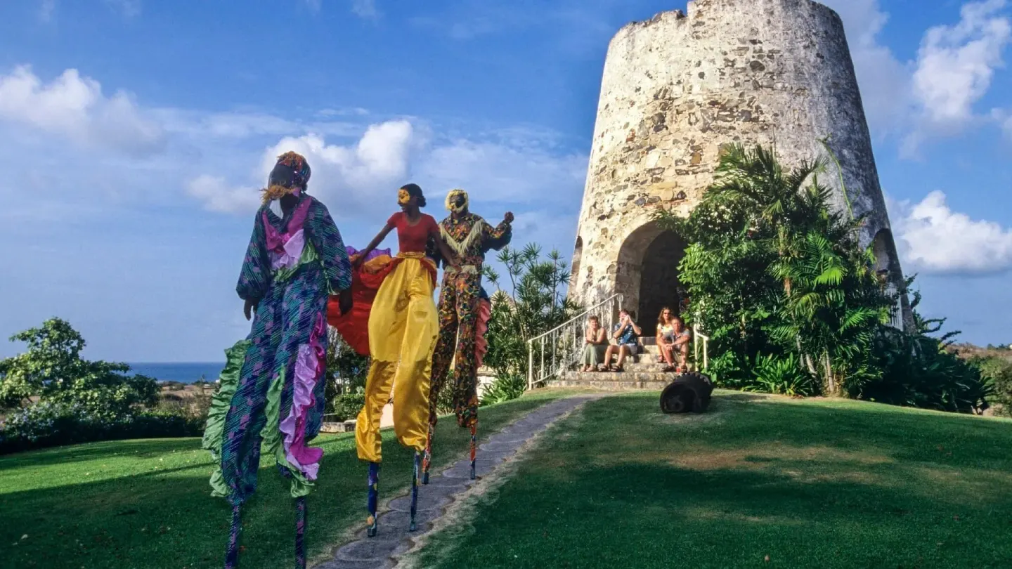 Stilt walkers beside a historic stone tower at The Buccaneer Beach & Golf Resort.
