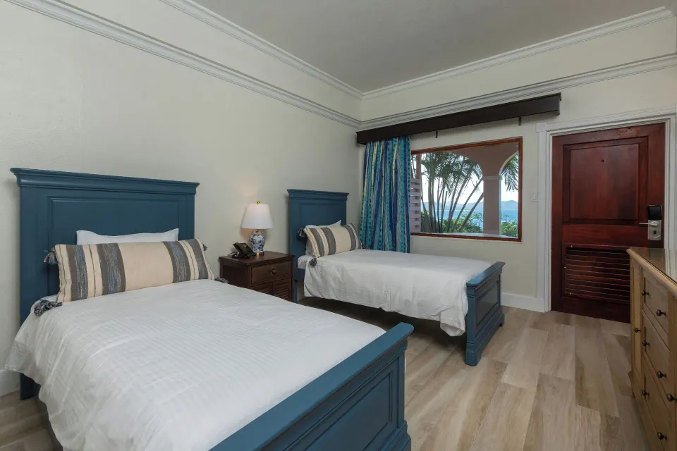 Family Cottage Suite bedroom with two beds and a window view at The Buccaneer Beach & Golf Resort.