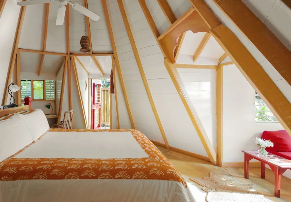 A bright A-frame guest room with a bed and red seating at The Caves.