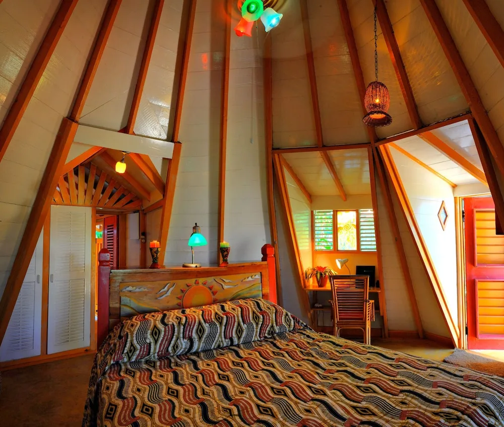 A colorful A-frame guest room with a bed, painted headboard, and open red door at The Caves.