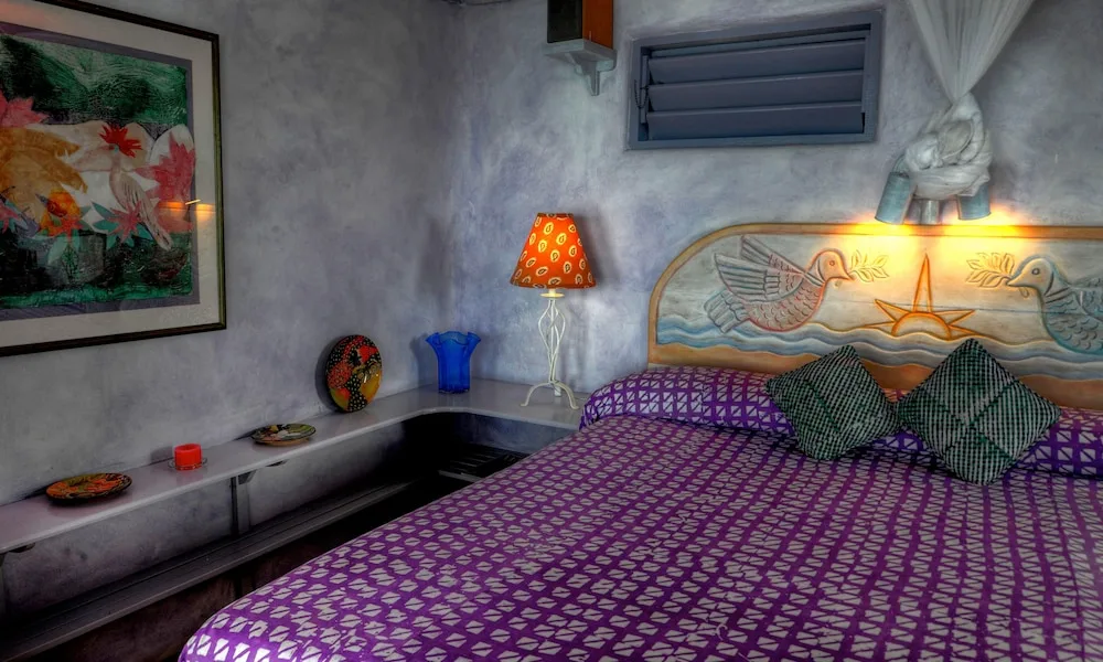 Colorful guest room bed with carved headboard and artwork at The Caves.