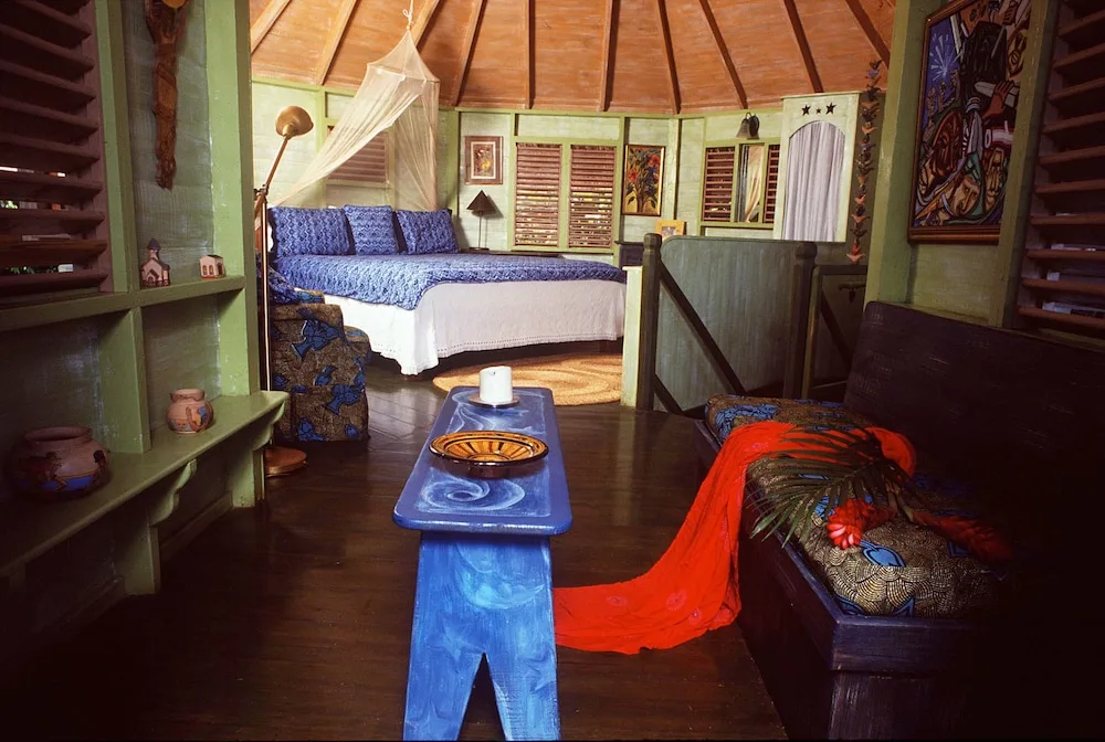 Guest room at The Caves with a blue-dressed bed, mosquito net, bench, and painted wood furnishings.