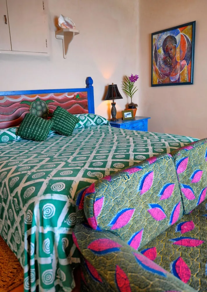 Guest room at The Caves with a green patterned bed, blue bedside table, artwork, and armchair.