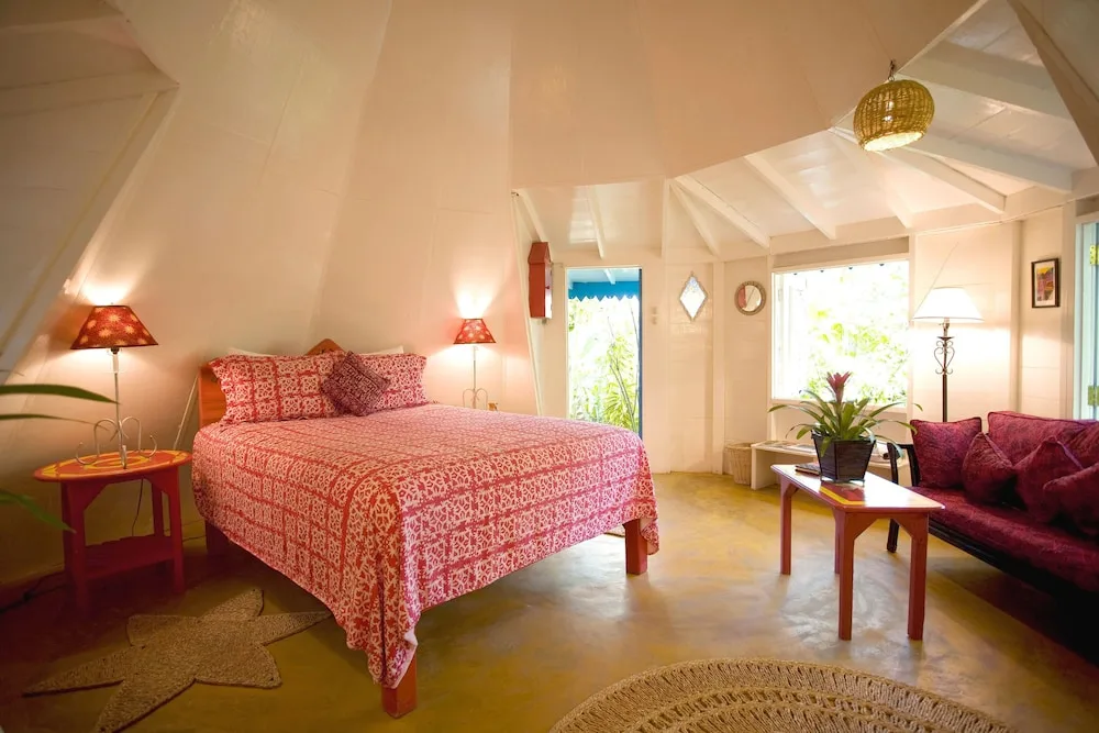 Guest room at The Caves with a red patterned bed, sofa, lamps, coffee table, and garden-facing windows.