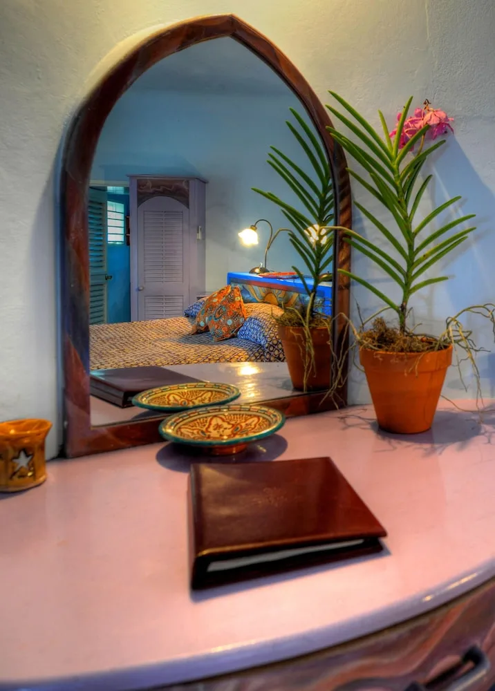 Guest room vanity at The Caves with an arched mirror, potted plants, and a bed reflected behind it.