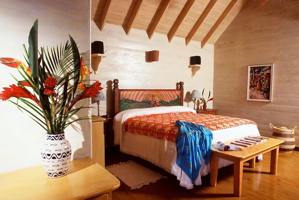 Guest room with a wooden bed, orange coverlet, and tropical flowers at The Caves.