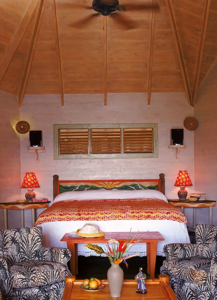 A high-ceiling guest room with a bed, armchairs, and red bedside lamps at The Caves.
