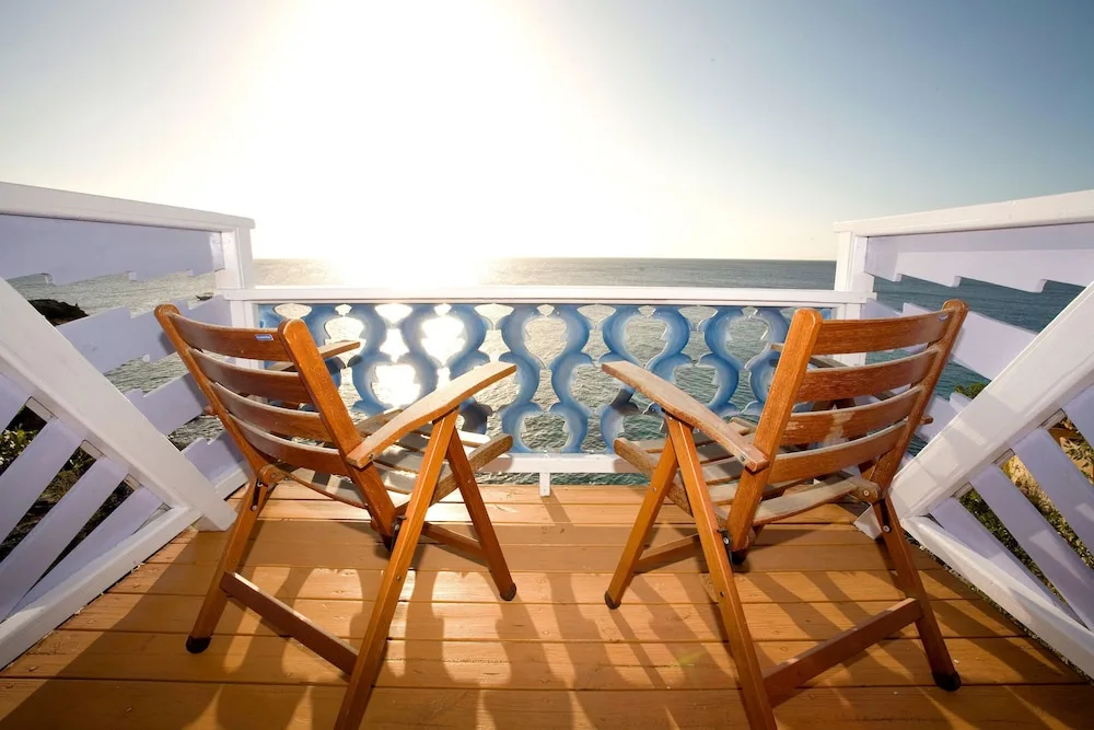 Two wooden chairs on a balcony facing the bright ocean at The Caves.