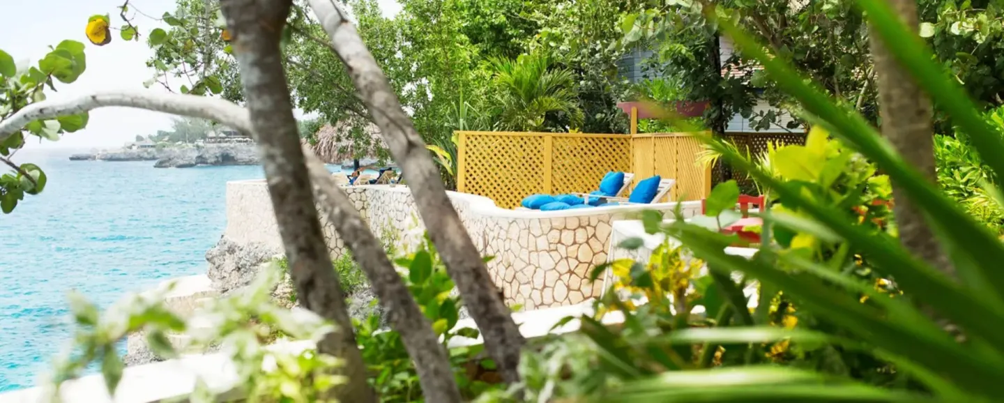 Seaside stone terrace with blue lounge cushions framed by greenery at The Caves.