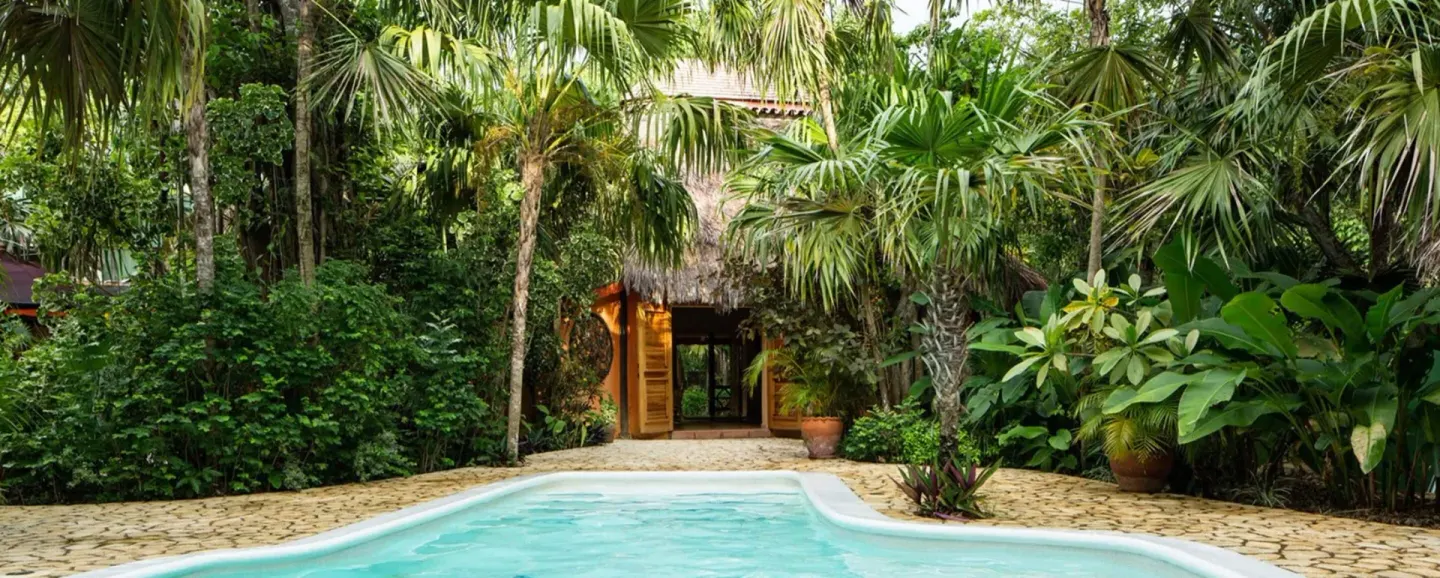 Pool with tropical foliage and a thatched building entrance at The Caves.