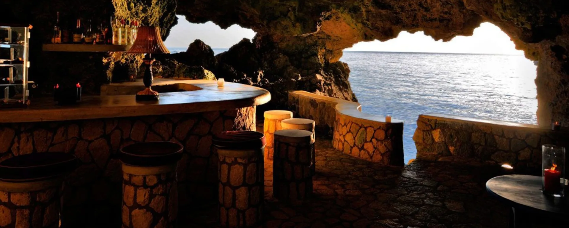 Cave bar with stone stools and ocean views through cliff openings at The Caves.