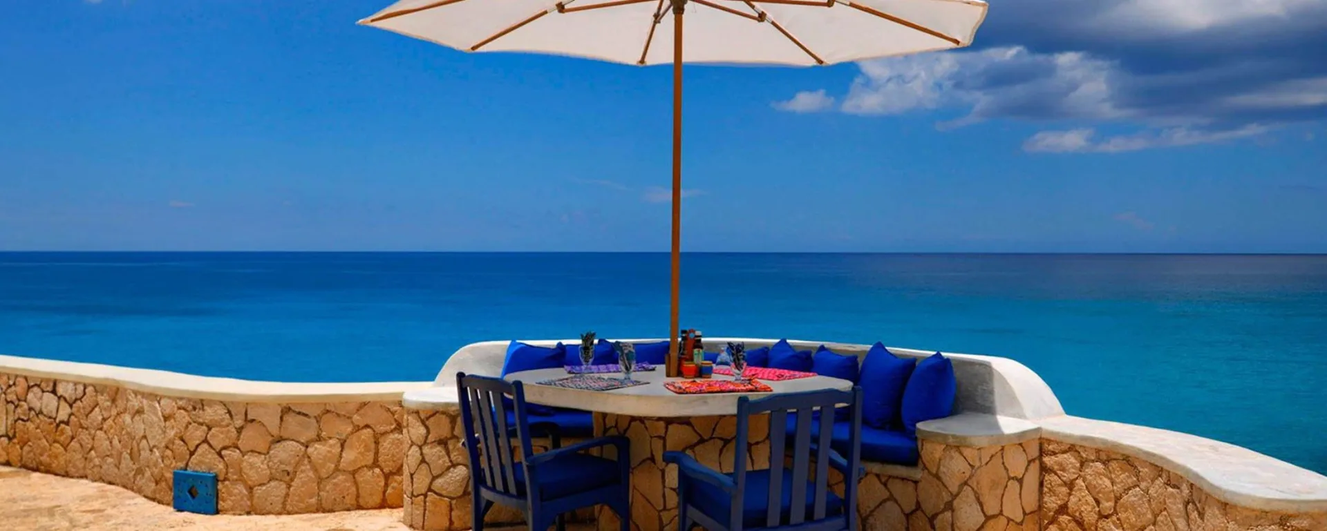 Oceanfront dining table under a white umbrella on a stone terrace at The Caves.