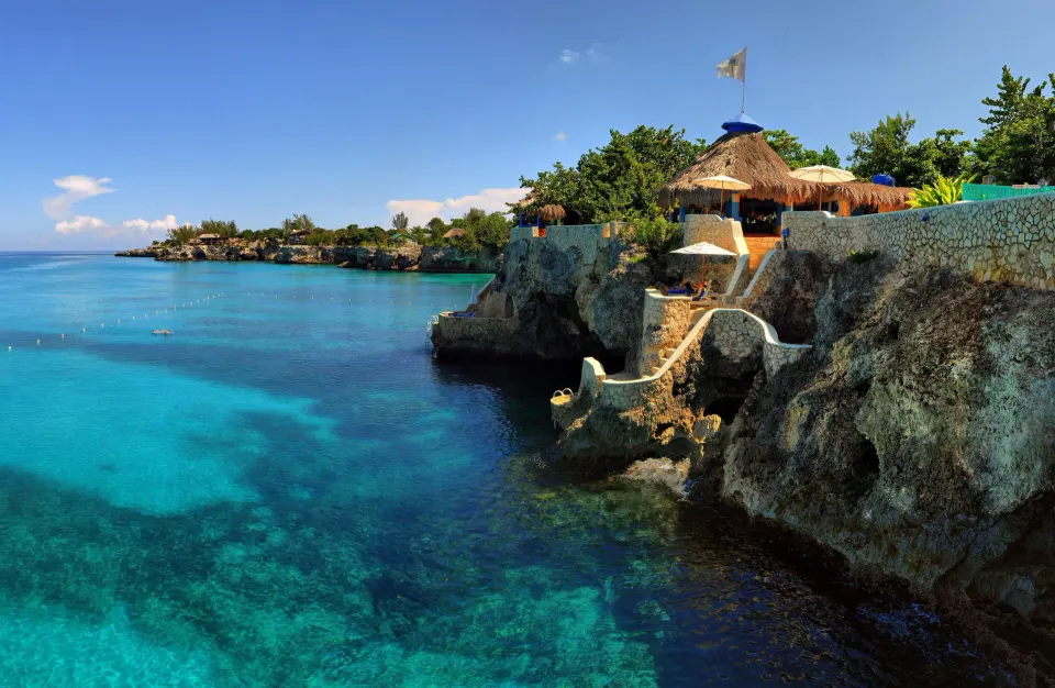 Cliffside ocean view with turquoise water and thatched cottages at The Caves.