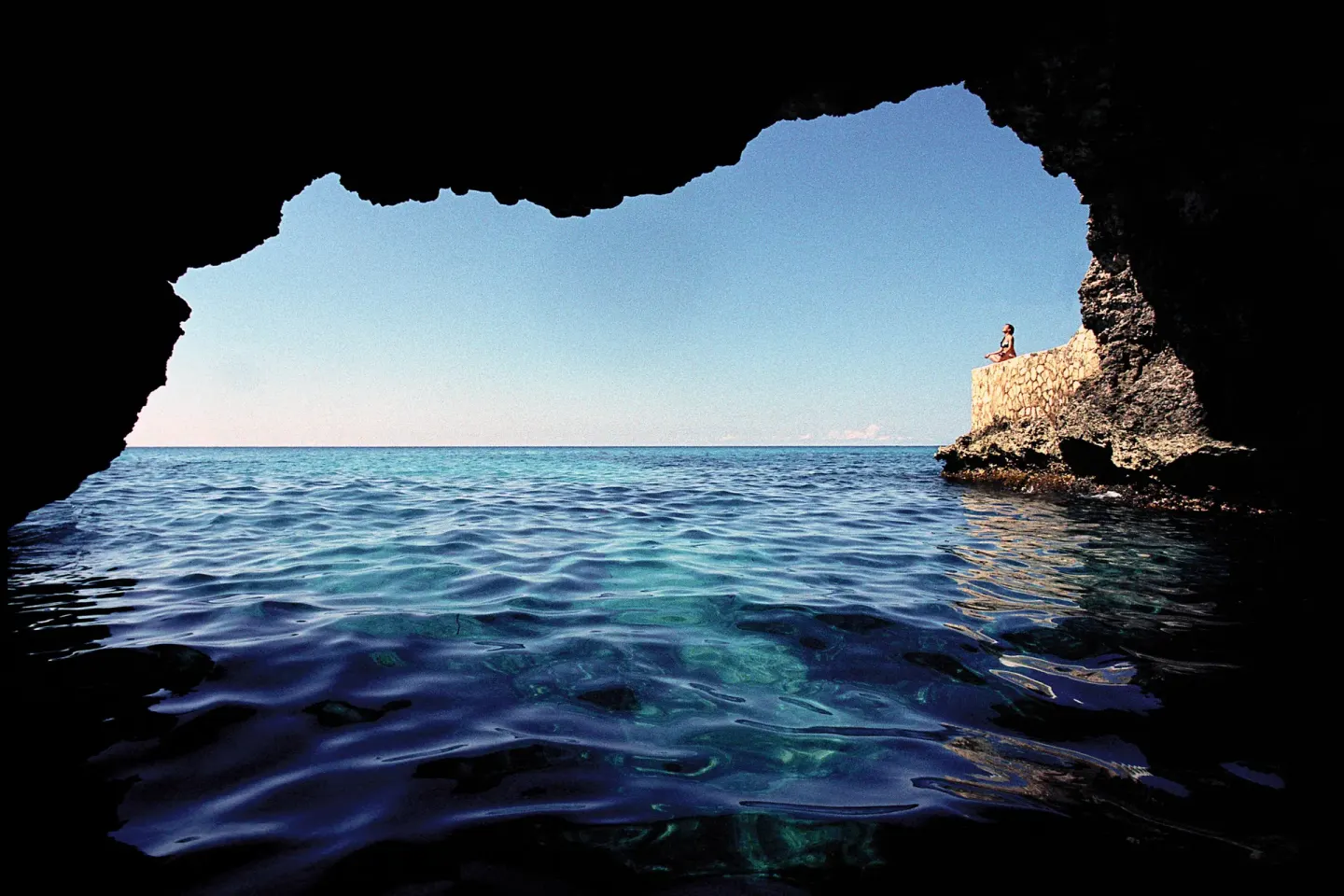 Ocean cave opening with blue water and cliffside stone wall at The Caves.