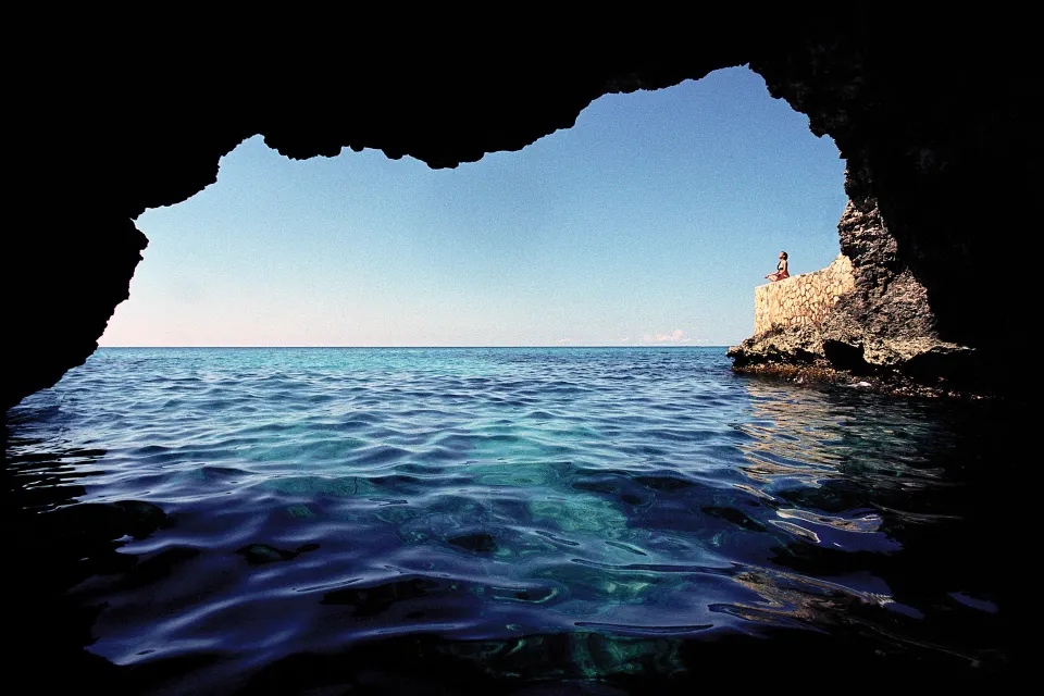 Ocean cave opening with blue water and cliffside stone wall at The Caves.