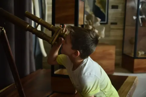 Child looks through a brass telescope display at The Club at Solaz.