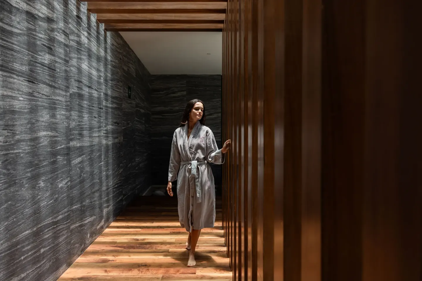 Woman in a robe walking through a dark stone spa corridor at The Club at Solaz.