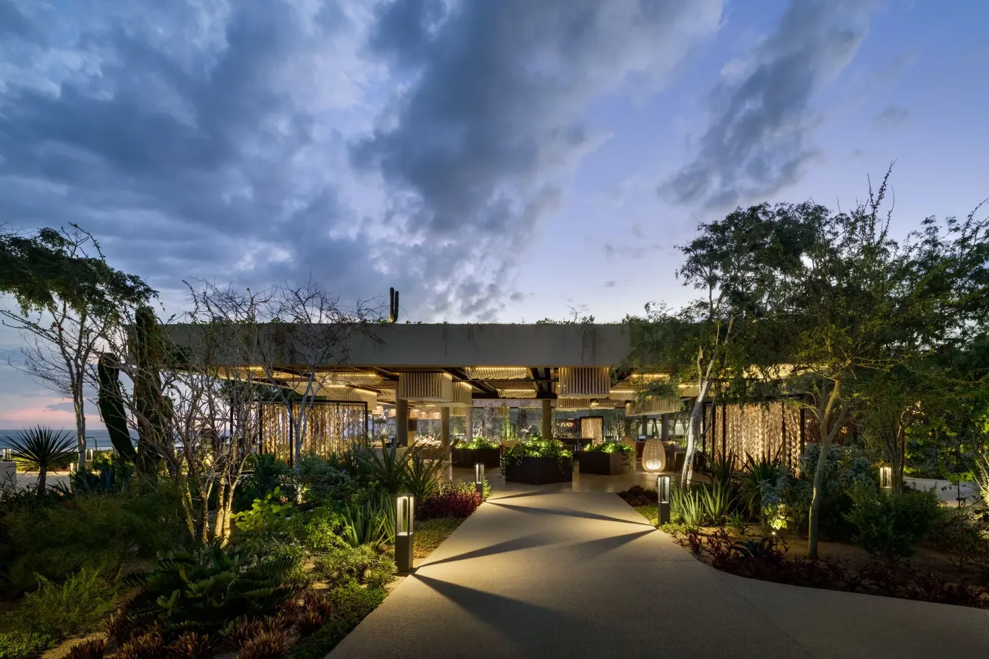 A landscaped walkway leads to a glowing open-air pavilion at The Club at Solaz.