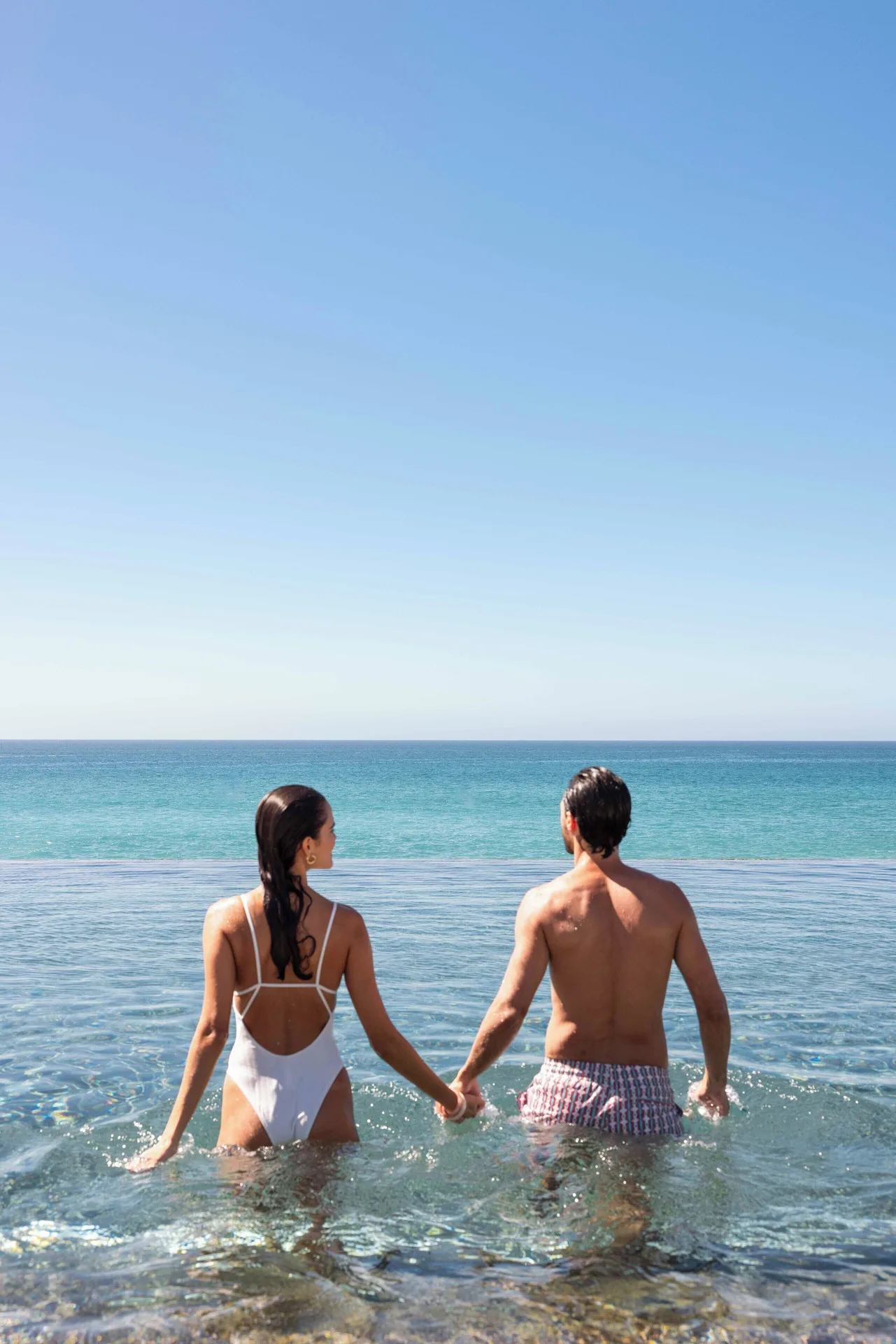 Two guests hold hands in an infinity pool overlooking the ocean at The Club at Solaz.