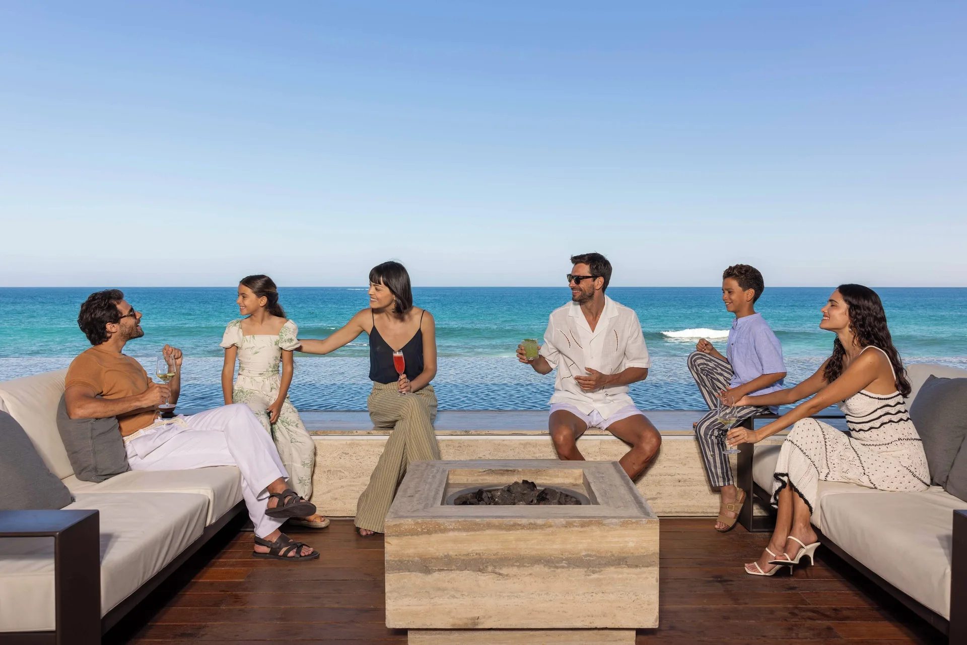 Guests seated around a square fire table beside the ocean at The Club at Solaz.
