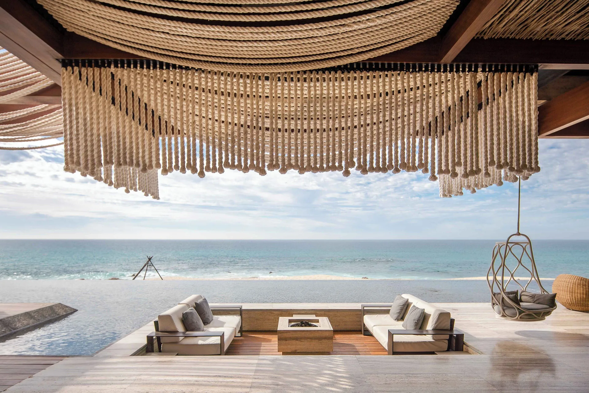 Open-air lounge with rope ceiling decor, sofas, pool edge and ocean view at The Club at Solaz.