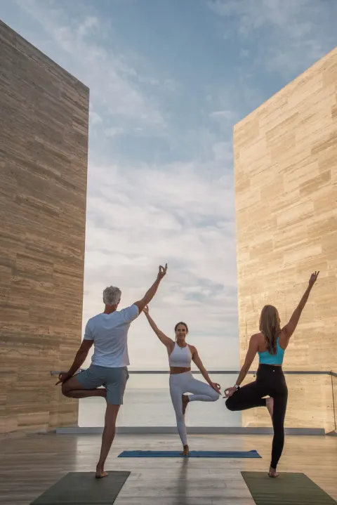 Three people practicing yoga between stone walls by the sea at The Club at Solaz.