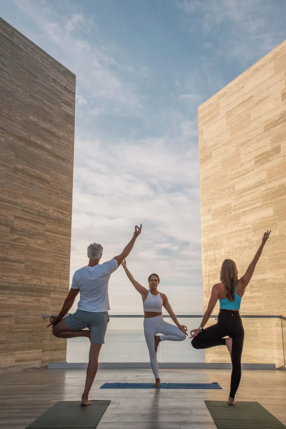 Three people practicing yoga between stone walls by the sea at The Club at Solaz.