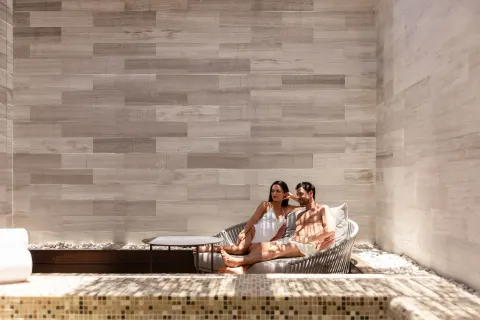 Couple relaxing on a cushioned lounger beside a mosaic pool at The Club at Solaz.