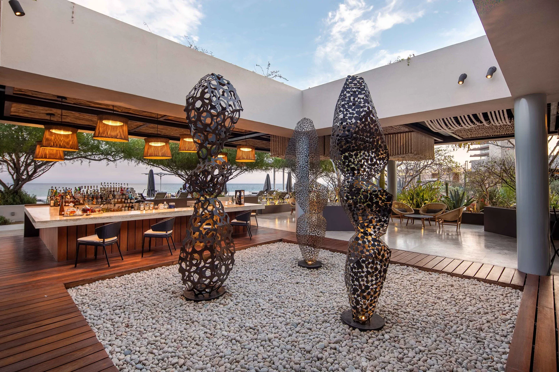 An open-air bar with sculptural art and ocean beyond is shown at The Club at Solaz.