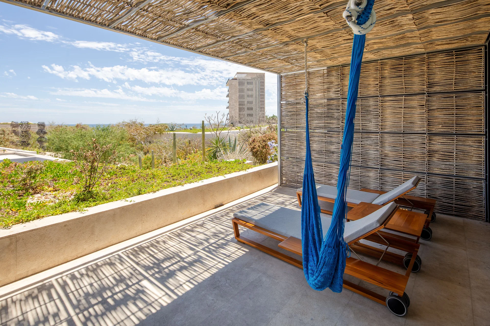 Shaded villa terrace at The Club at Solaz with blue hammock, loungers, greenery, and ocean beyond.