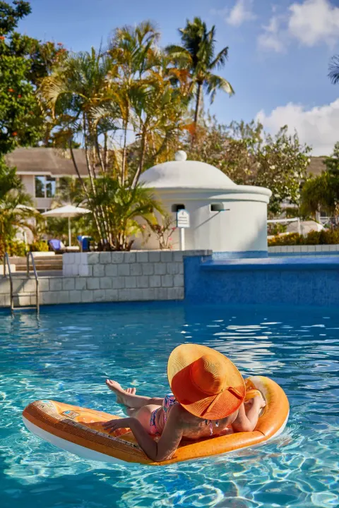 Guest floating on an orange pool lounger at The Club, Barbados Resort & Spa.