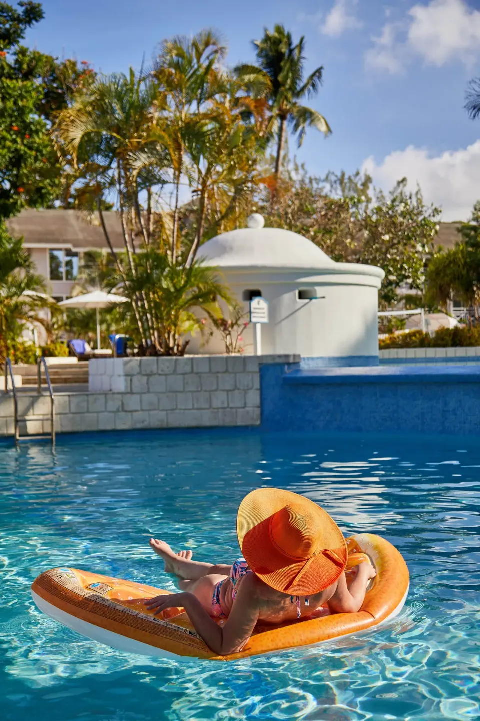 Guest floating on an orange pool lounger at The Club, Barbados Resort & Spa.
