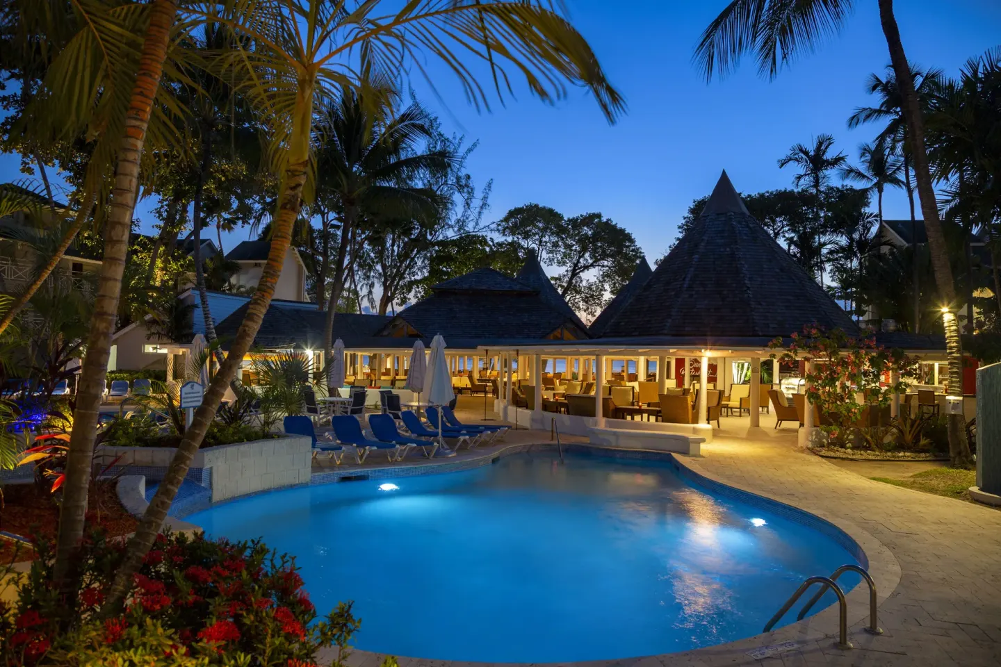 Illuminated pool and open-air dining pavilion at dusk at The Club, Barbados Resort & Spa.