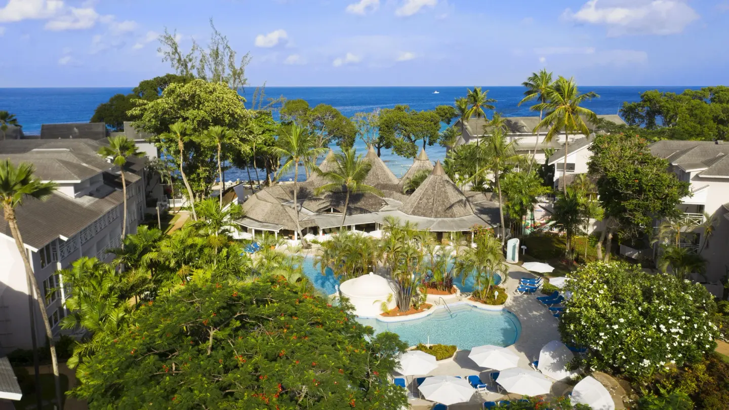Aerial view of pools, palms, and the ocean at The Club, Barbados Resort & Spa.