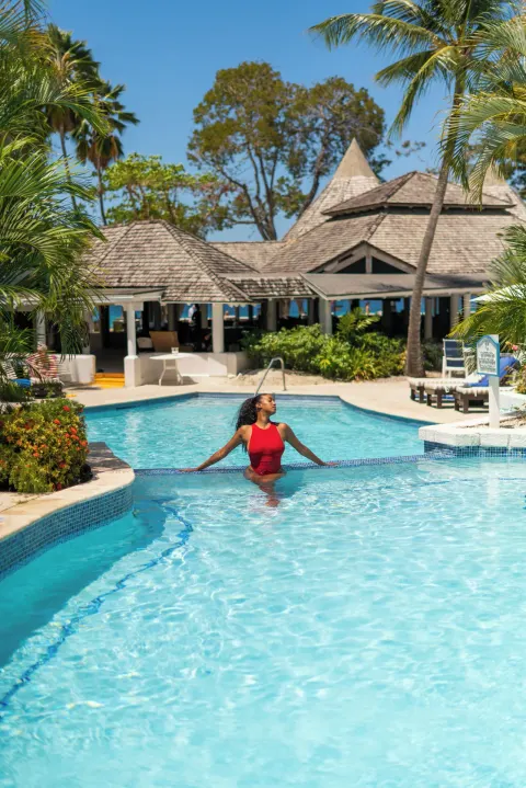 Guest standing in the resort pool with tropical landscaping at The Club, Barbados Resort & Spa.