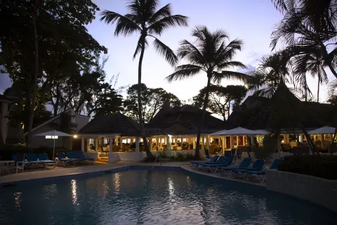 Pool with palm silhouettes and lit dining pavilion at twilight at The Club, Barbados Resort & Spa.