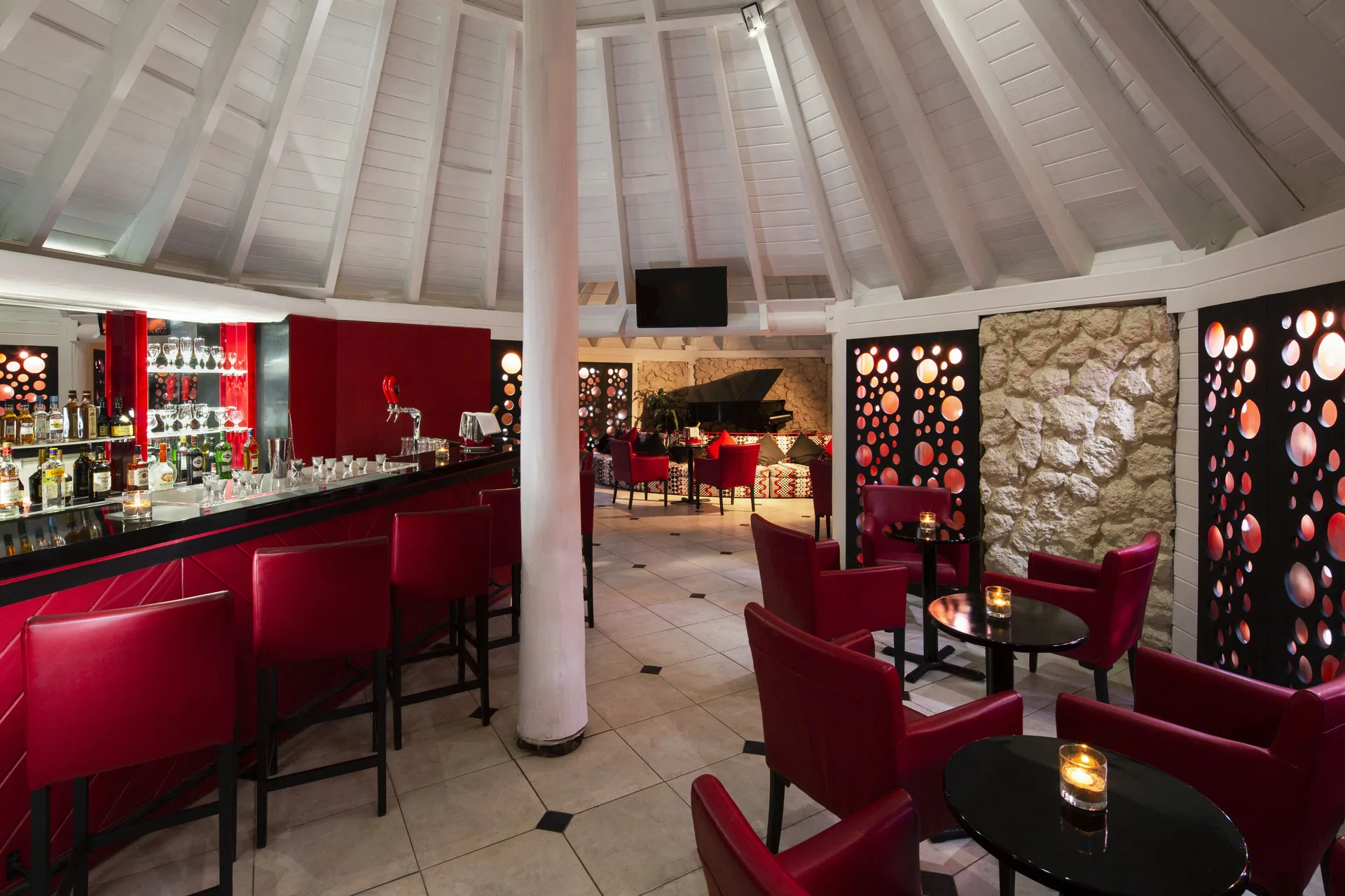 Lounge bar with red chairs and a piano at The Club, Barbados Resort & Spa.