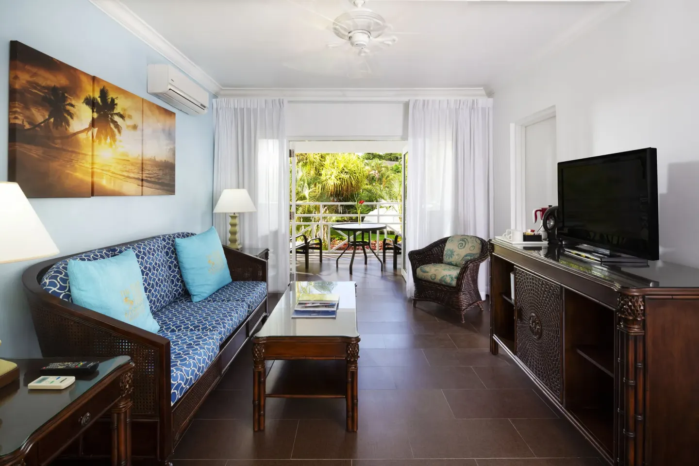 One Bedroom Garden View Suite living room with sofa, TV and balcony at The Club, Barbados Resort & Spa.