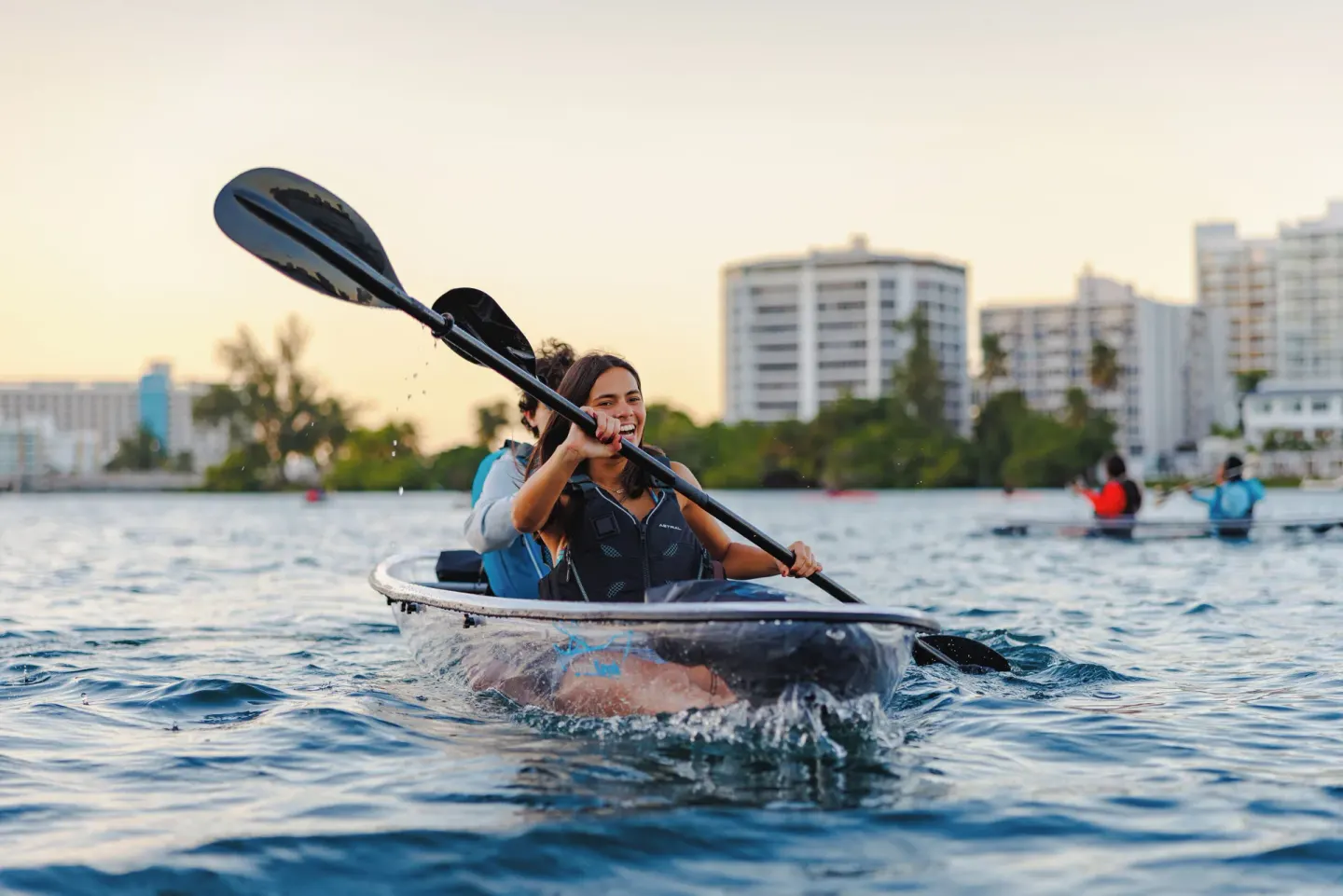 A smiling kayaker paddles a clear kayak on the lagoon at The Condado Plaza Hotel.