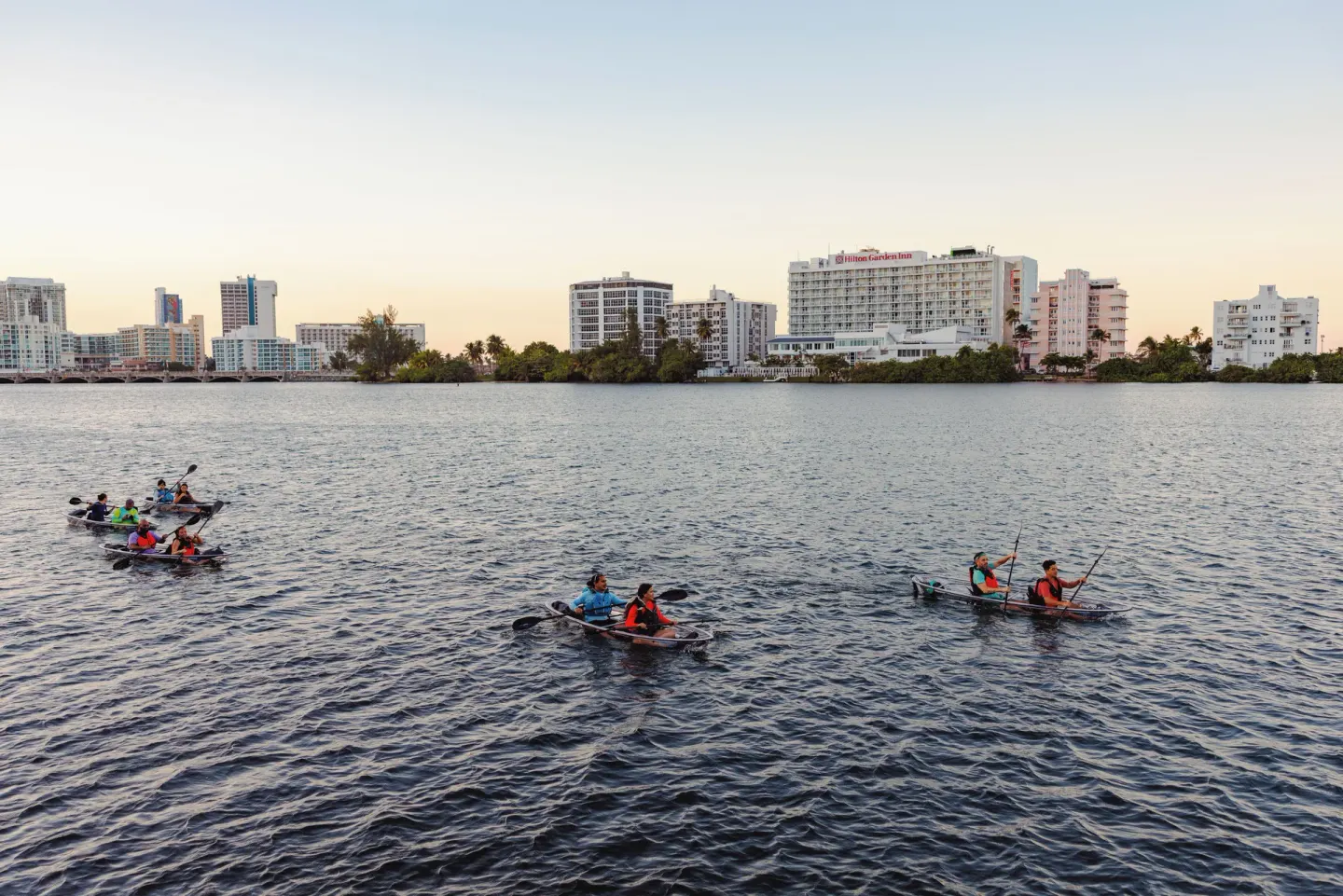 Several kayaks cross the lagoon with The Condado Plaza Hotel in the distance.