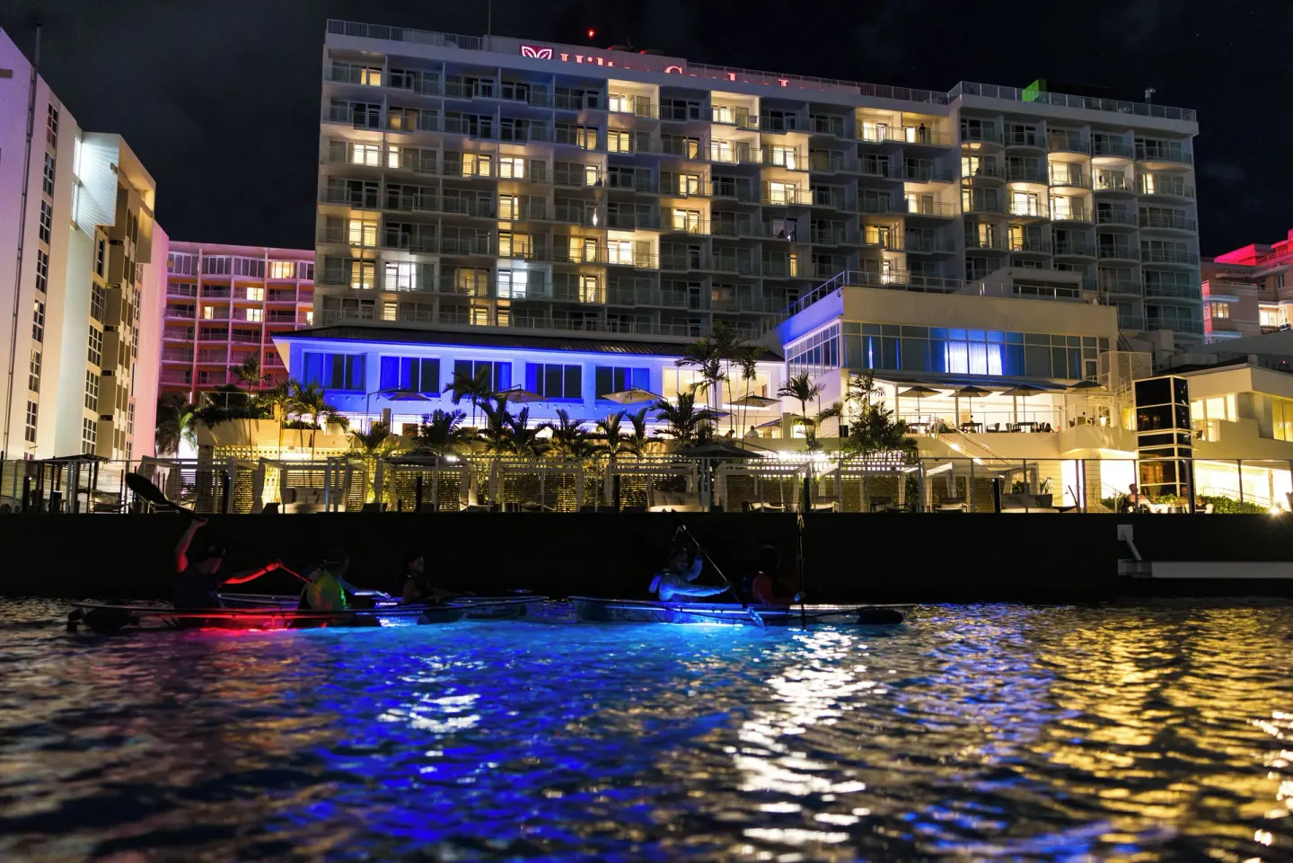 Lighted kayaks float on the lagoon beside The Condado Plaza Hotel at night.